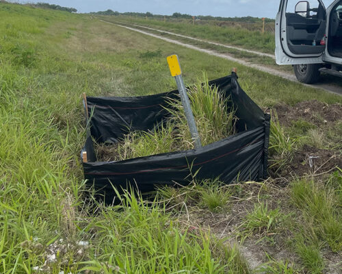 Bent yellow marker in silt fence, tall grass, open car door.