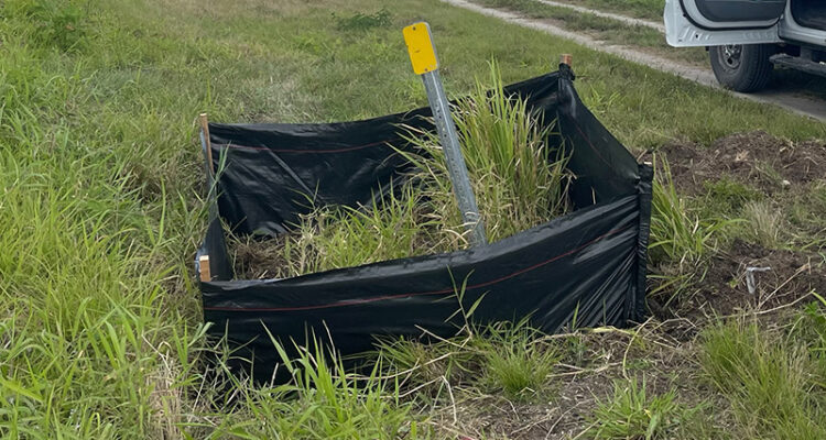 Bent yellow marker in silt fence, tall grass, open car door.
