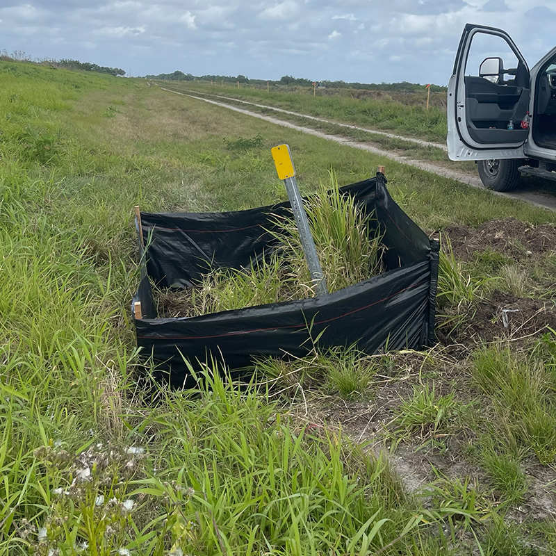 Bent yellow marker in silt fence, tall grass, open car door.