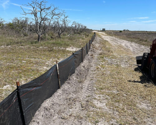 Black silt fence lines dirt path in dry, open field.