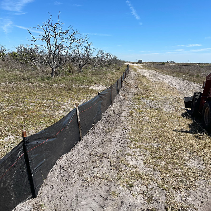 Black silt fence lines dirt path in dry, open field.