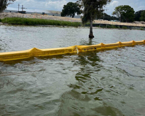 Yellow floating barrier by a submerged tree under cloudy skies.
