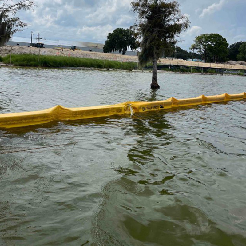 Yellow floating barrier by a submerged tree under cloudy skies.