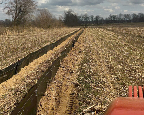 Plowed field with silt fence, crop stubble, and tractor.