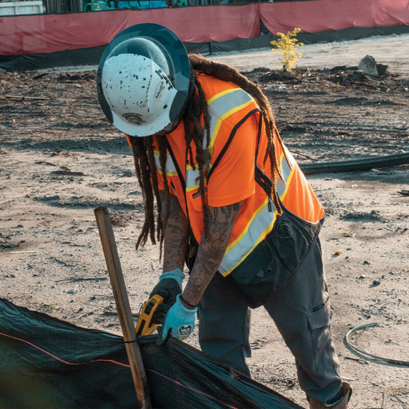 Worker in safety gear secures black material with a tool.