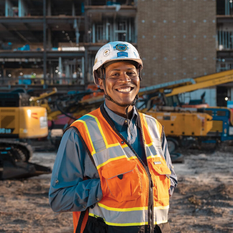 Smiling construction worker in hard hat and vest onsite.