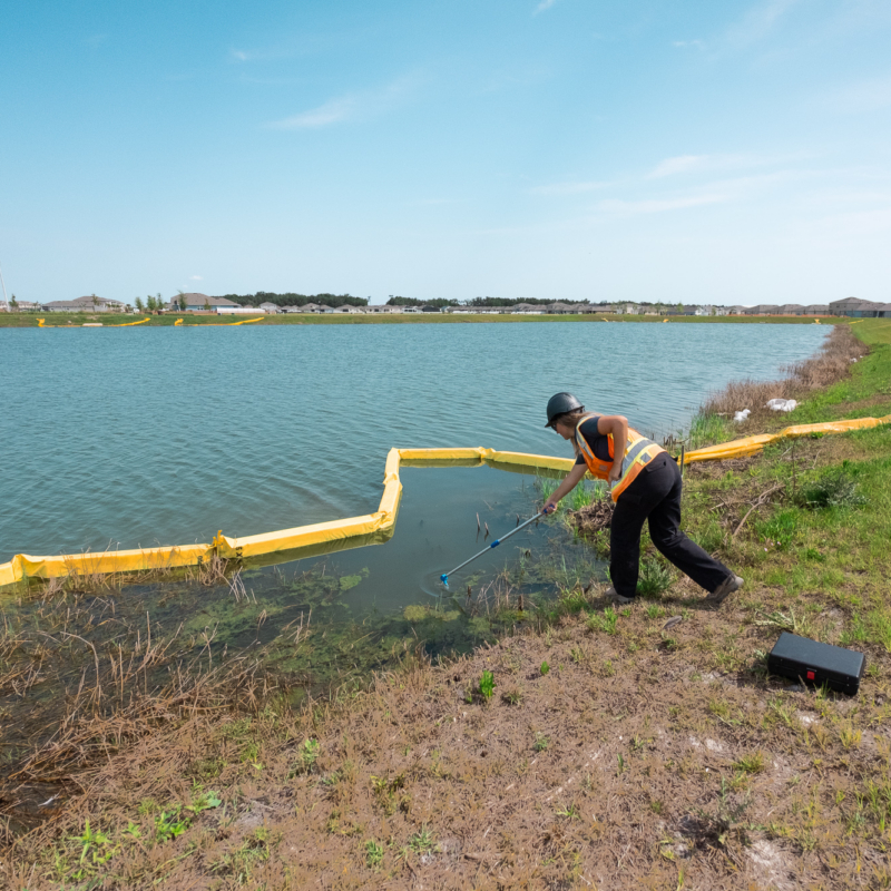 Person in safety gear samples water by a yellow barrier.