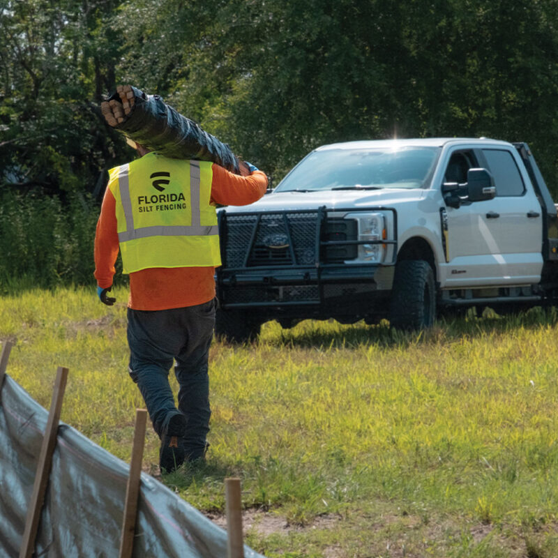Worker in Florida Silt Fencing vest carries posts to pickup truck.