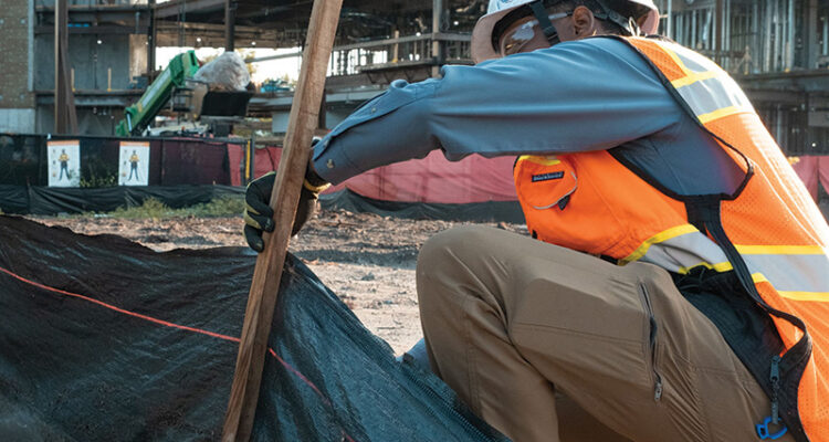 Worker in safety gear installs stake at construction site.