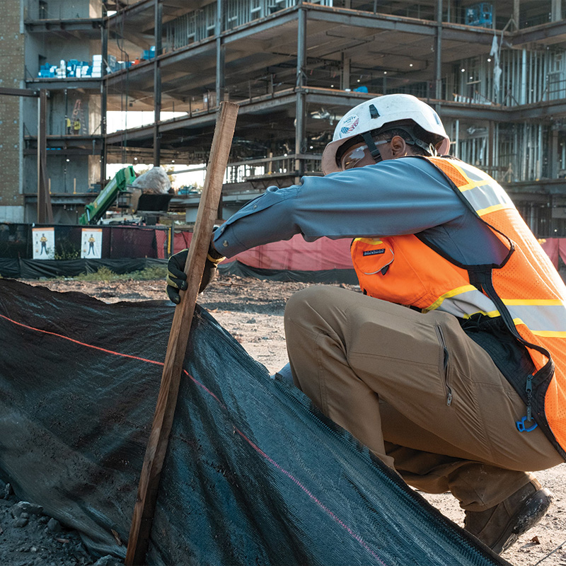 Worker in safety gear installs stake at construction site.