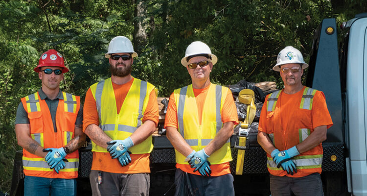 Four construction workers in safety gear stand by a work truck.