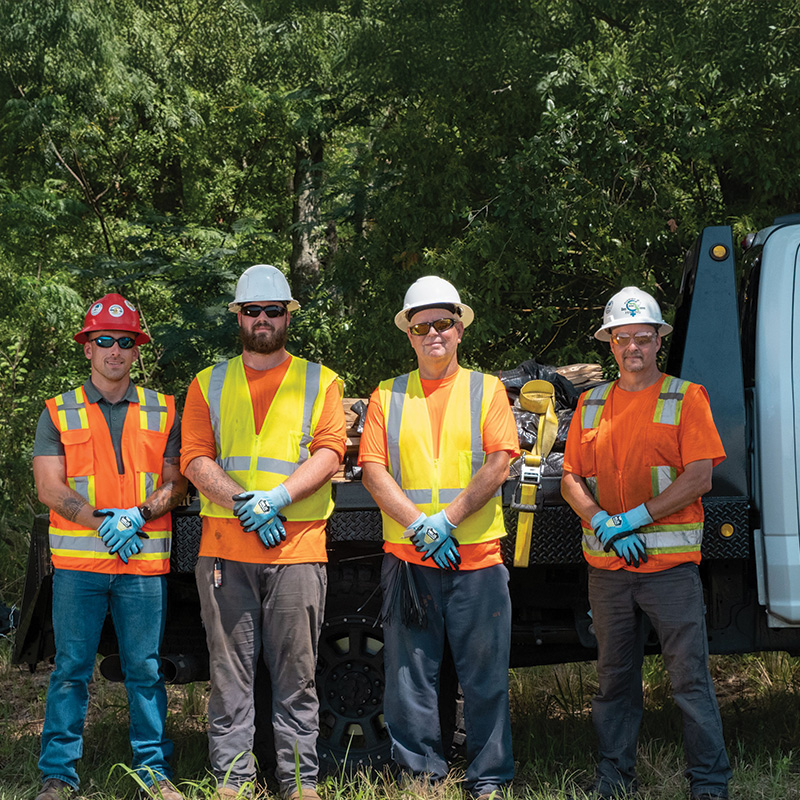 Four construction workers in safety gear stand by a work truck.